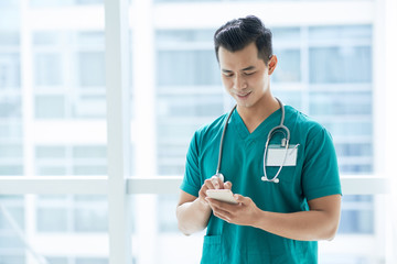Smiling handsome Asian doctor reading text message in his smartphone