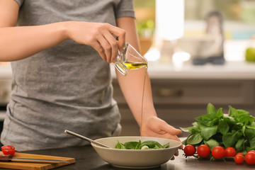 Woman pouring oil onto fresh salad with basil at table