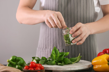 Woman putting fresh green basil into glass jar at table
