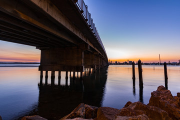 Obraz premium Sun setting over bridge and lake with reflection in water