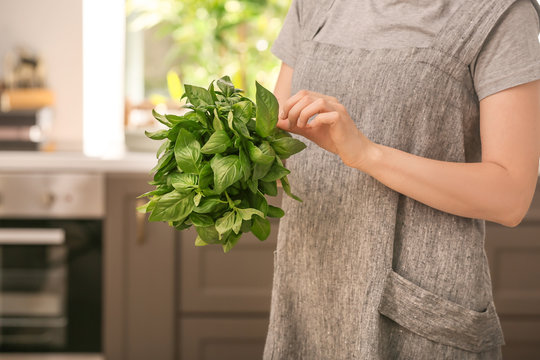 Woman with bunch of fresh green basil in kitchen