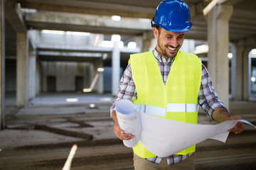 Portrait of male site contractor engineer with hard hat holding blue print paper