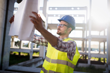 Fototapeta na wymiar Portrait of male site contractor engineer with hard hat holding blue print paper