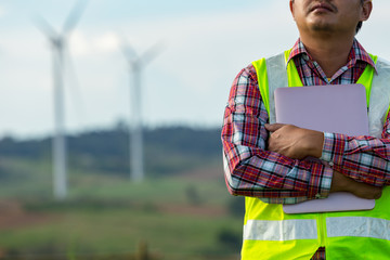 Engineering man standing holding laptop looking wind turbines clean energy project for produce...