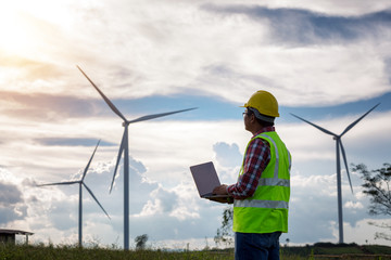 Engineering man standing holding laptop looking wind turbines clean energy project for produce...