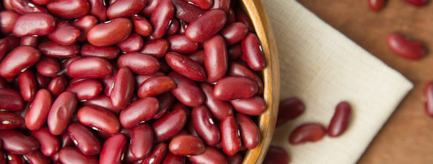 Close up of red beans in wooden bowl putting on linen and wooden background. Banner with copyspace.