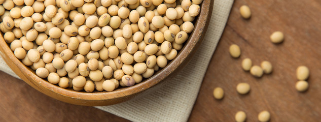 Close up of soybeans in wooden bowl putting on linen and wooden background. Banner with copyspace.