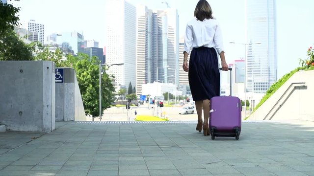 Businesswoman with suitcase walking in city
