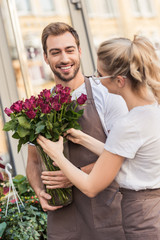 happy young florists holding burgundy roses near flower shop