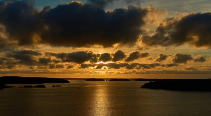 Golden sunset over sea coast with reflection of sunlight on water. Sun behind the clouds. 