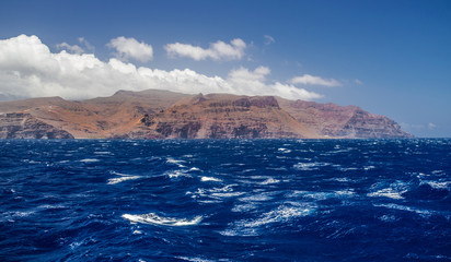 Fototapeta na wymiar La Gomera island volcanic coastline view with waves and blue sky and clouds, Canary islands, Spain