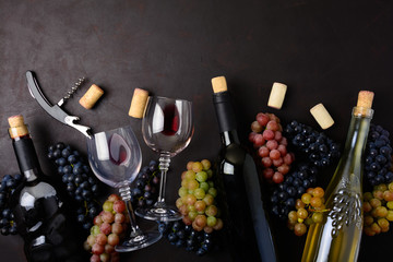 Wineglasses with red and white wine, bottles, grapes, corkscrew and corks lying on dark wooden background. Top view. Flat lay. Copy space