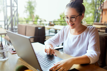 Young mixed race woman working with laptop in cafe at tropical location. Asian caucasian female studying using internet. Business woman doing social marketing work and shopping. Telecommuting concept.