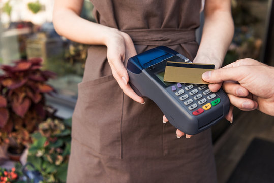cropped image of customer paying with credit card at flower shop, florist holding payment terminal
