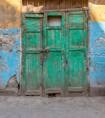 Closed green wooden grunge weathered abandoned door on dirty wall painted in yellow and blue colors
