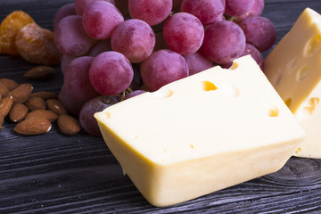 Cheese cuts with figs, nuts, honey, grapes on a dark rustic wooden boards background