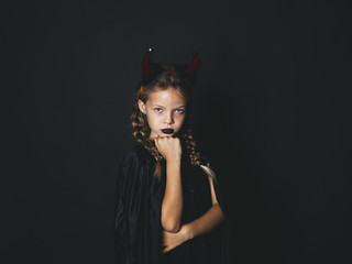 beautiful young girl with red halloween horns and cape in front of black background