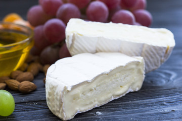 Cheese cuts with figs, nuts, honey, grapes on a dark rustic wooden boards background