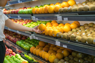 Fresh healthy fruits on shelves in supermarket. With a woman hand choosing best fruits