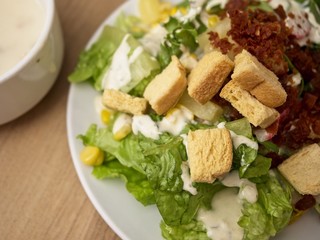 Mix salad that consists of mixed vegetables fruits and meats in white plate on wooden table