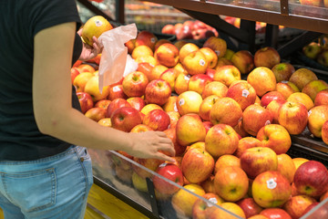 Fresh healthy fruits on shelves in supermarket, with female buyer choosing red apples