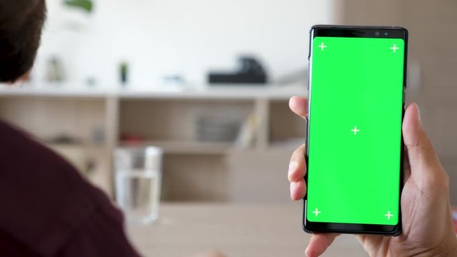Close up of man hand touching and using a smartphone with green screen chroma mock up on it in the living room of his house