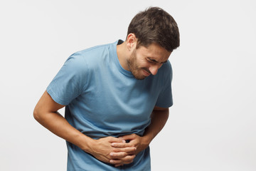 Young man touching his stomach isolated on gray background space. Abdominal pain or ache concept