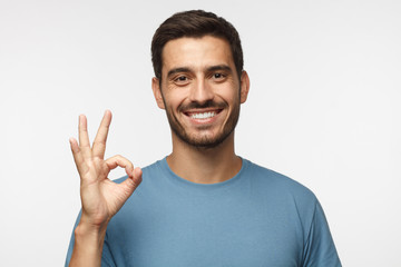 Young man in blue t-shirt having happy look, smiling, gesturing, showing OK sign. Caucasian male...