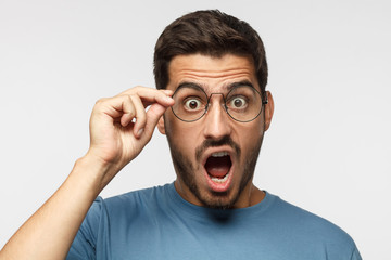 Angry young teacher in blue t-shirt shouting, displeased with bad behaviour, holding round...