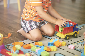 Little Asian child playing with lots of colorful plastic blocks indoor. Kid boy wearing colorful shirt and having fun with building and creating.