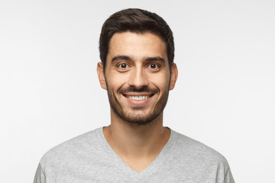 Close up portrait of young smiling handsome guy in gray t-shirt isolated on gray background