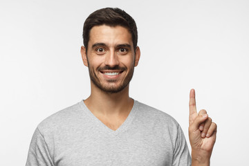 Handsome young man pointing up with his index finger, isolated on gray background