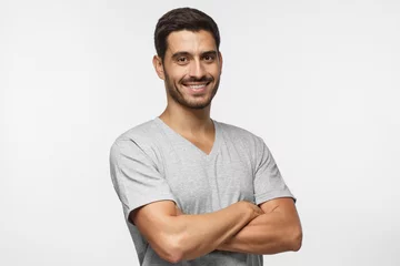 Foto op Canvas Portrait of attractive young sporty man in gray t-shirt standing with crossed arms isolated on grey background © Damir Khabirov