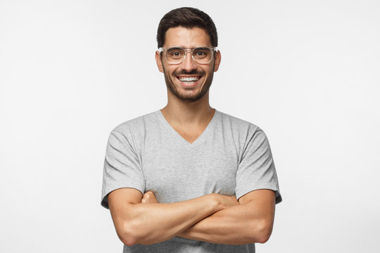 Laughing handsome man in transparent glasses standing with crossed arms isolated on gray background