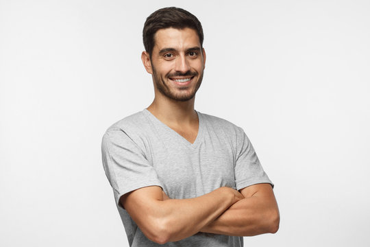 Portrait of attractive young sporty man in gray t-shirt standing with crossed arms isolated on grey background