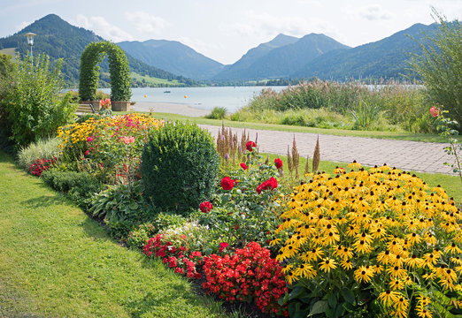 Wunderschöner Kurpark am Schliersee mit Sommer Blumenbeet und Bogen. Blick in die bayerischen Alpen