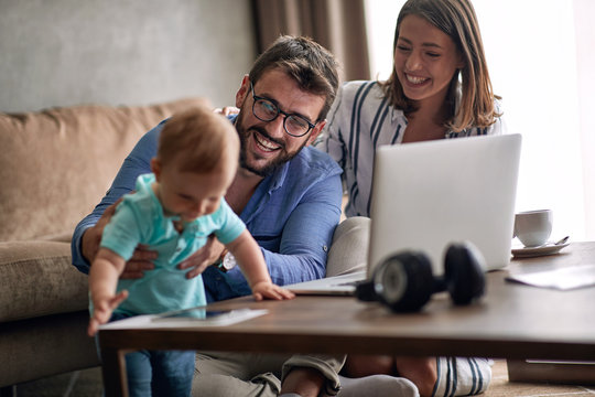 Couple with baby working from home using laptop.