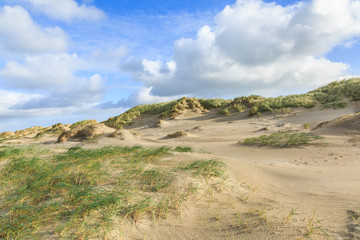 Dune valleys with deep wind holes carved out by heavy storm with swaying marram grasses with scattered clouds against blue sky