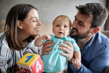family, parenthood and people concept – young mother and father kissing little baby at home.