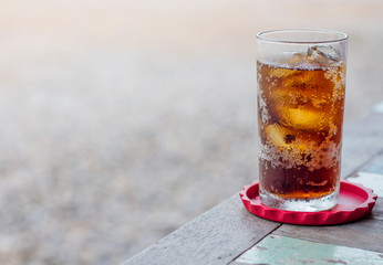 glass of cola or coke with ice cubes on a wooden