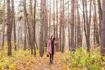 Fototapeta premium Autumn, fashion, people concept - woman with brown retro suitcase walking through the autumn park and smiling