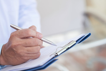 Close-up of male doctor holding pen and writing a prescription paper in clipboard