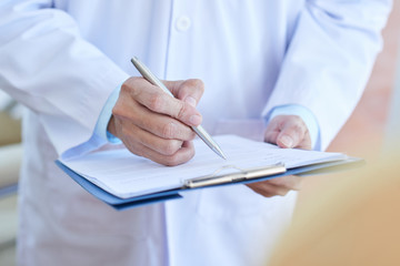 Close-up of male doctor in lab coat filling in medical form or prescribing a medicine