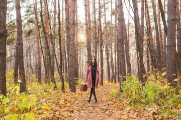Fototapeta premium Autumn, season and people concept - woman in pink coat with brown case standing in autumn park over the nature background