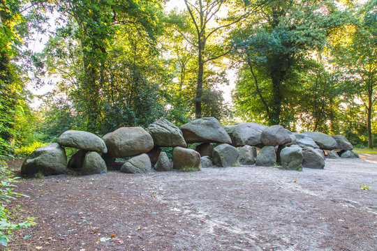 Dolmen D27 in the Dutch province of Drenthe with a background of oak trees and lights of the rising sun . A dolmen is construction work from the new stone age