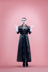 Fototapeta premium Halloween. Beautiful woman with bright black halloween makeup in a black leather cloak at pink studio