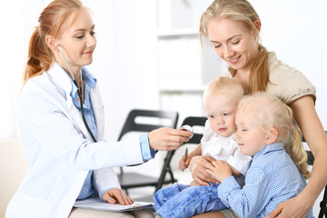 Fototapeta premium Doctor examining a little boy with stethoscope. Mother holds her son on her lap. Motherless and medicine concept