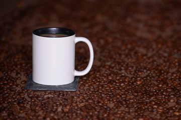 White mug of coffee with milk (Americano) stands at a table with coffee beans in the background with copy space
