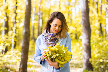 Fototapeta na wymiar Fall, nature and people concept - Young beautiful woman in grey coat holding autumn bouquet of leaves