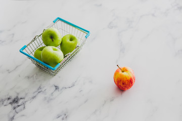 grocery store mini shopping basket with one single red apple among other green ones